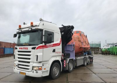 Autolaadkraan op industrieterrein met oranje valreddingsboot achterop